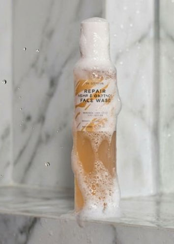 Woman applying skincare product to her face with a bottle of the product in the background.